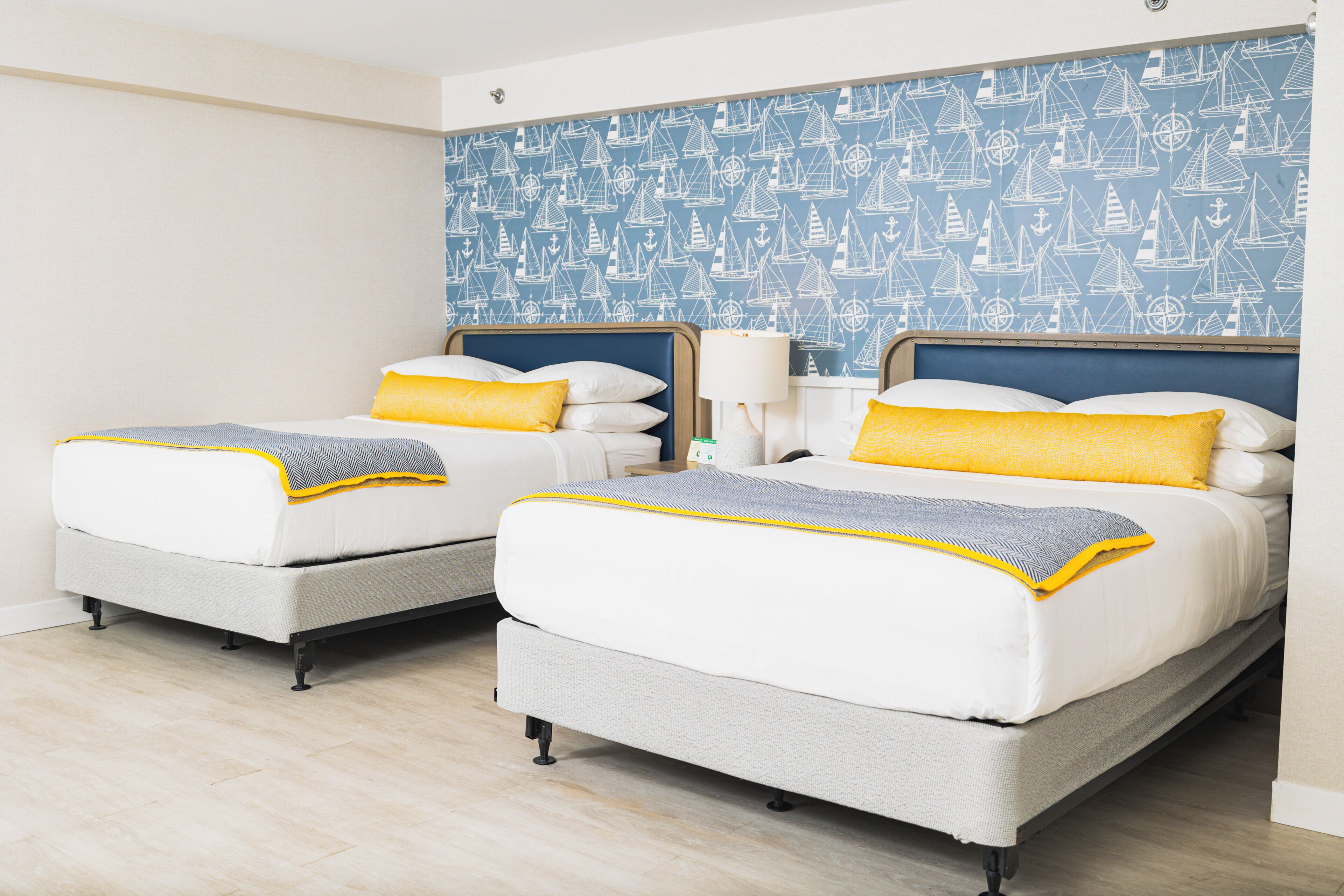 Habitación doble con dos camas, cada una con un colchón blanco y una manta amarilla.