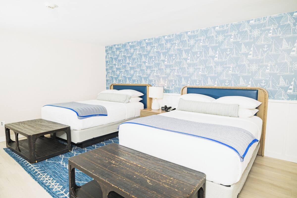 A hotel room with two beds, a small wooden table, and a patterned wall.