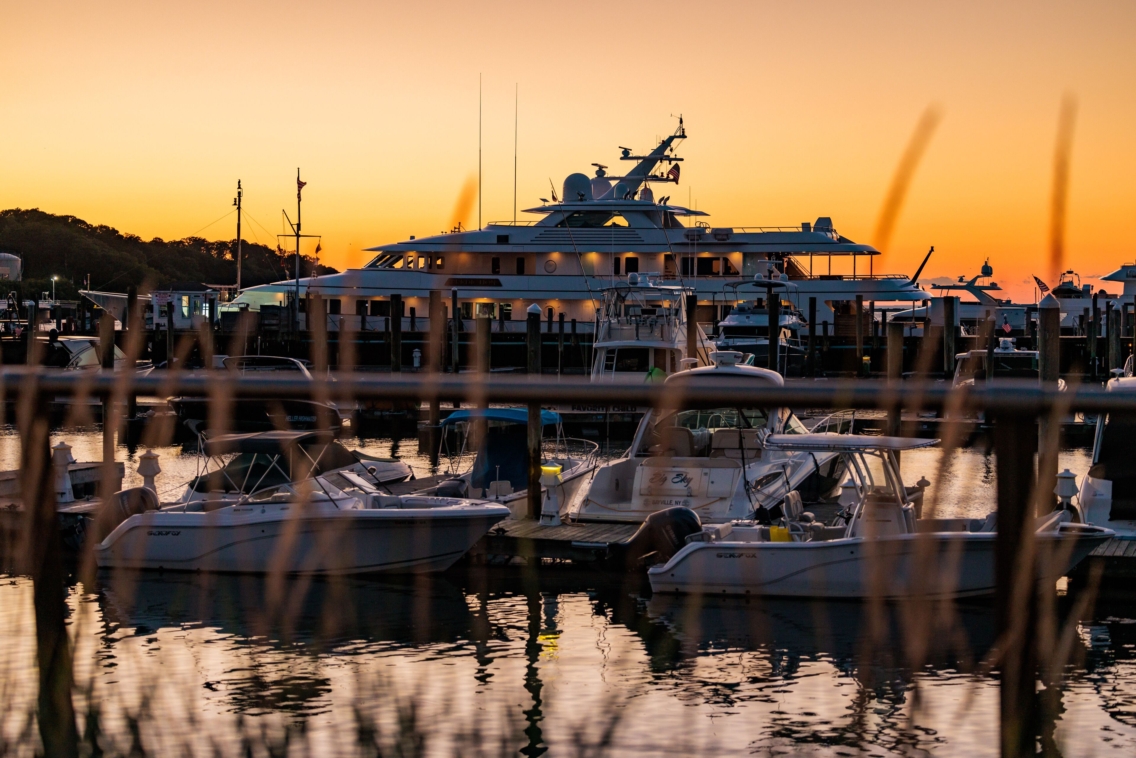 Een jachthaven met verschillende boten afgemeerd aan houten steigers, omgeven door kalm water dat de zonsondergang weerspiegelt.