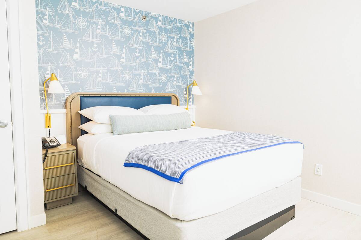 A neatly made bed with a blue and white patterned headboard, two bedside lamps, and a nightstand with a telephone.