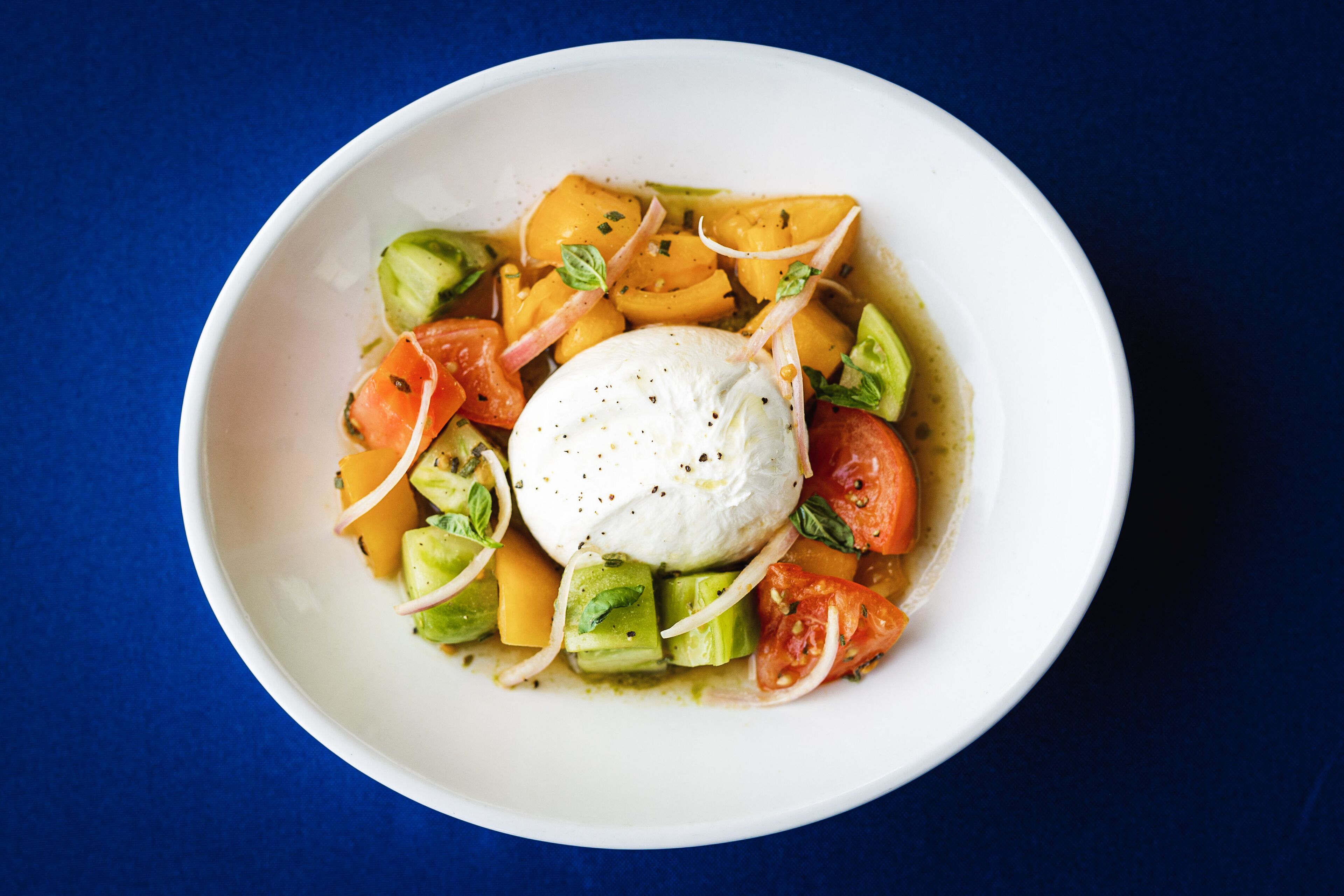 A bowl of food with avocado, tomatoes, and a poached egg on a blue background.