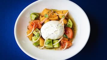 A bowl of food with avocado, tomatoes, and a poached egg on a blue background.