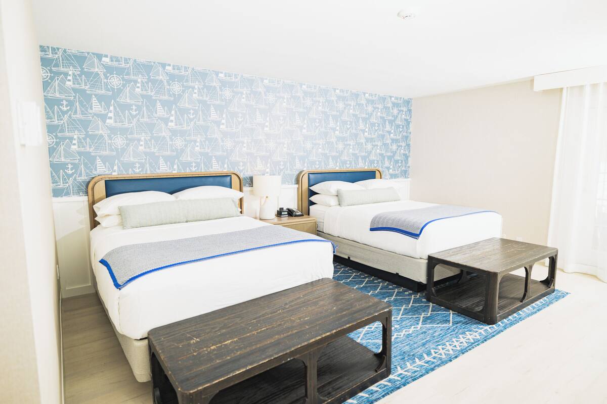 A hotel room with two beds, a nightstand, a wooden side table, and a patterned rug.