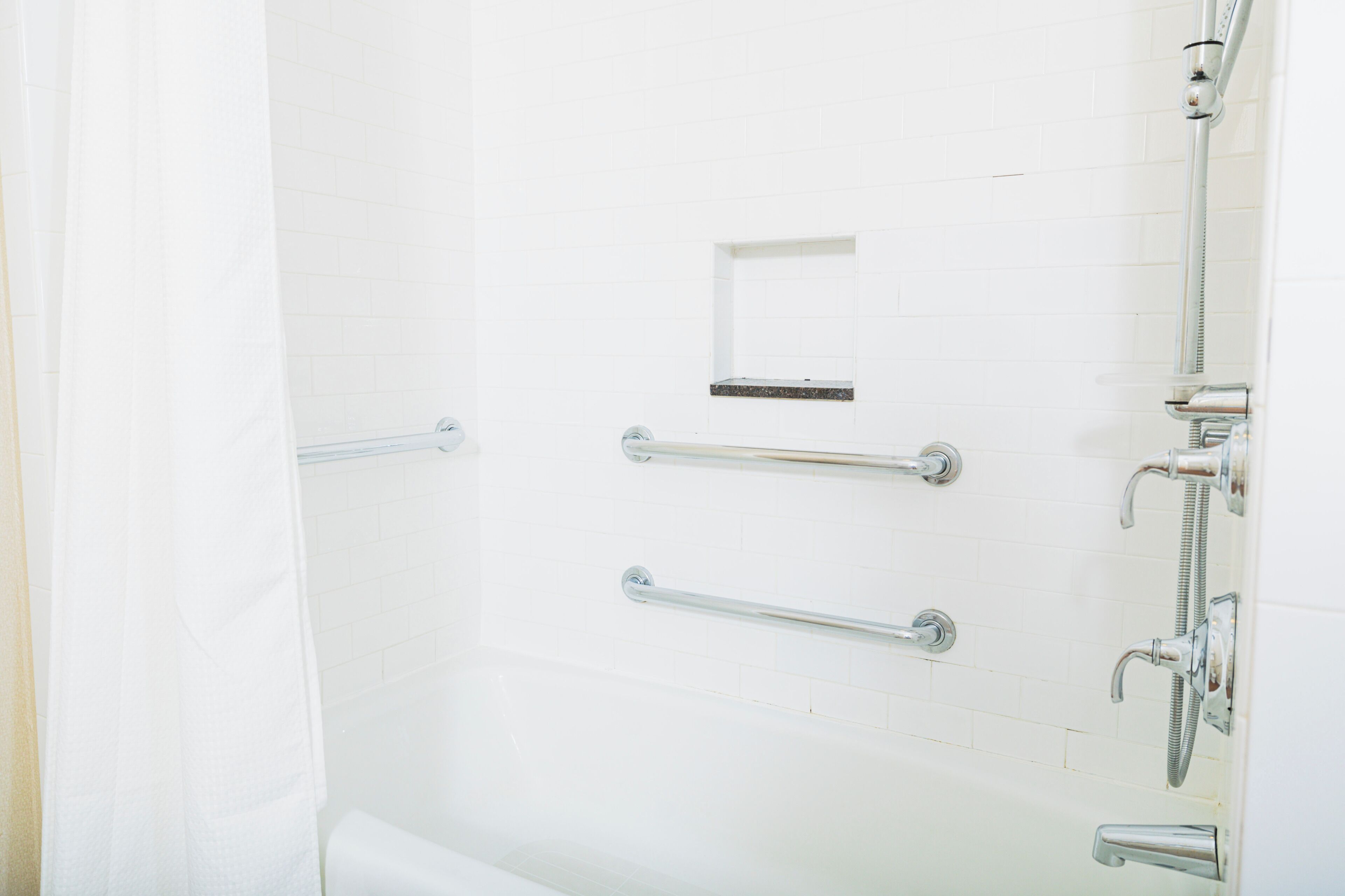 Een witte betegelde douche met handgrepen en een douchehouder.