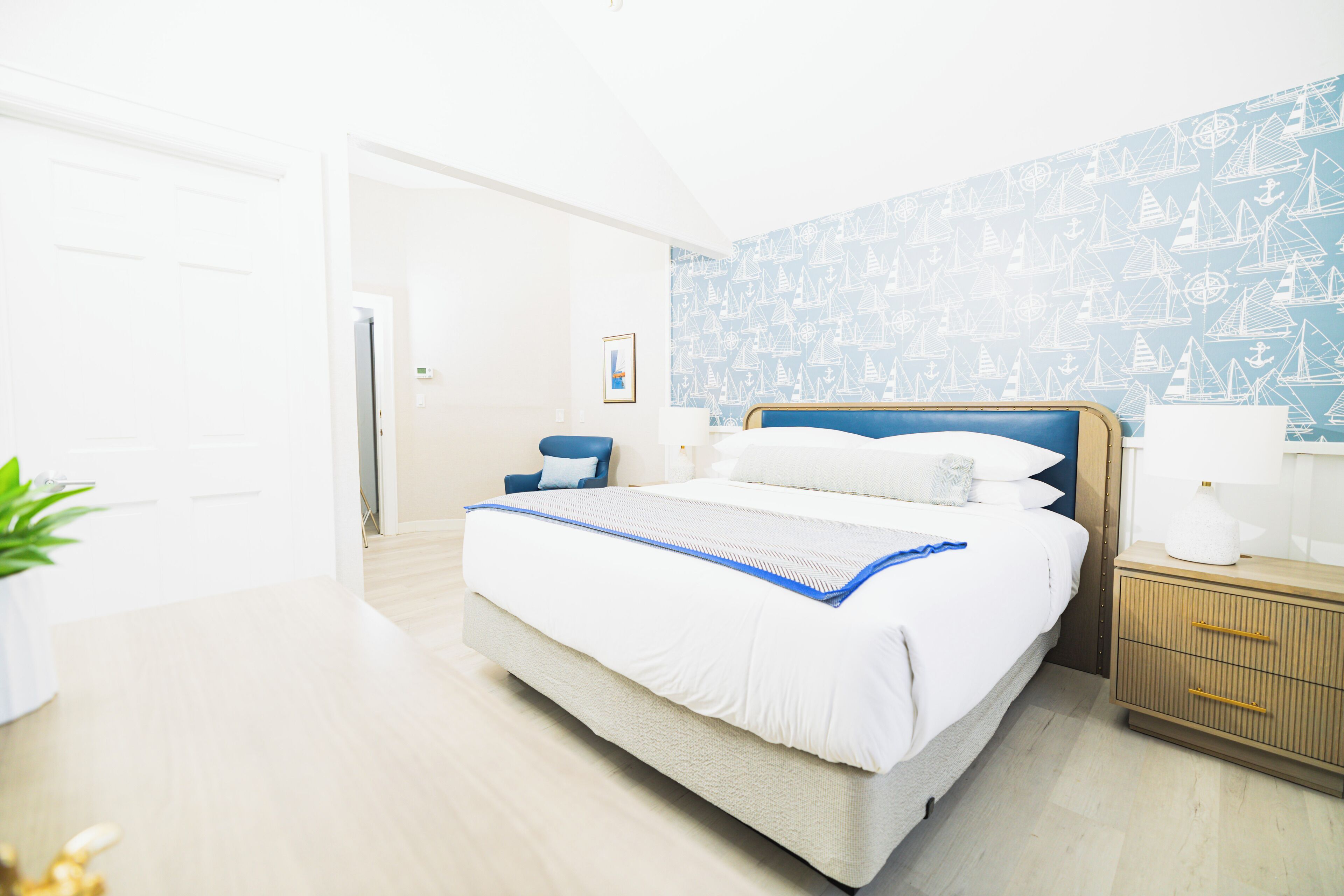 Une chambre d’hôtel moderne avec un grand lit, une table de chevet avec une lampe et un mur recouvert d’un papier peint sur le thème de la marine.