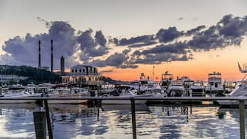 A marina with boats docked, a building with a red and white striped chimney, and a sunset in the background.