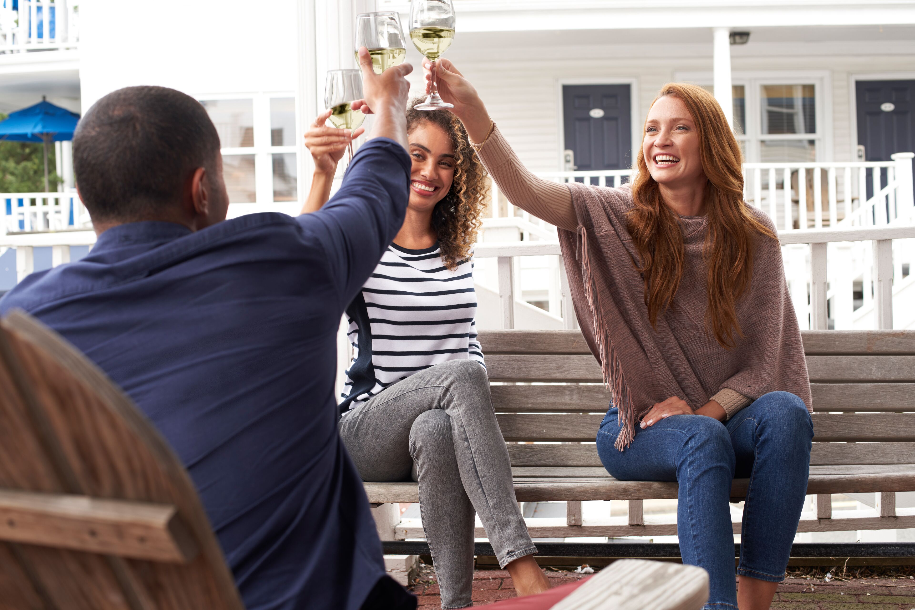 Un groupe de personnes trinquant avec des verres de vin sur une véranda dotée de balustrades blanches et d’une porte bleue.