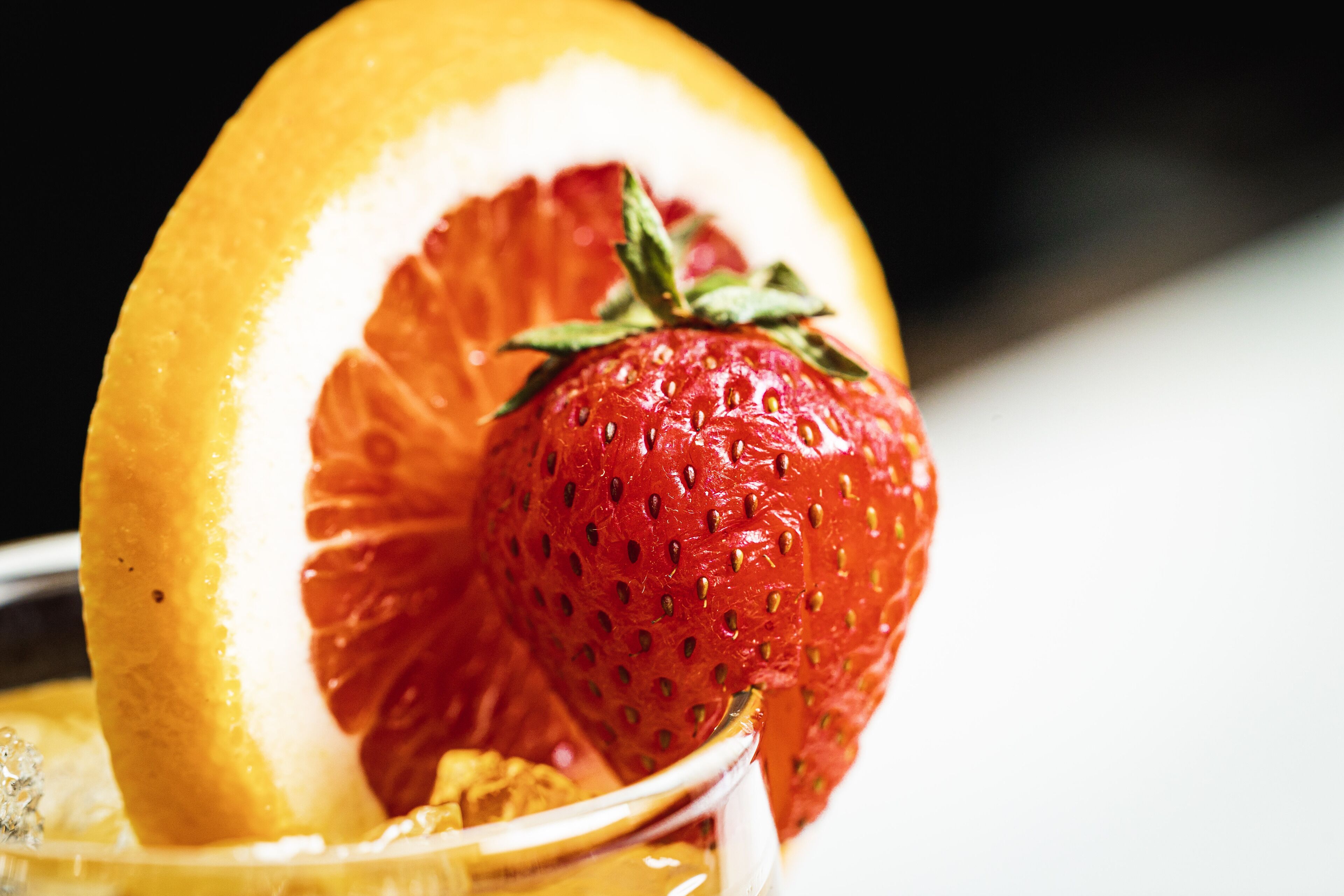 A close-up of a fruit garnish on a beverage, including a strawberry and a slice of orange.