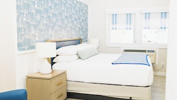 A neatly arranged bedroom with a bed, bedside table, lamp, and a wall with a nautical pattern.