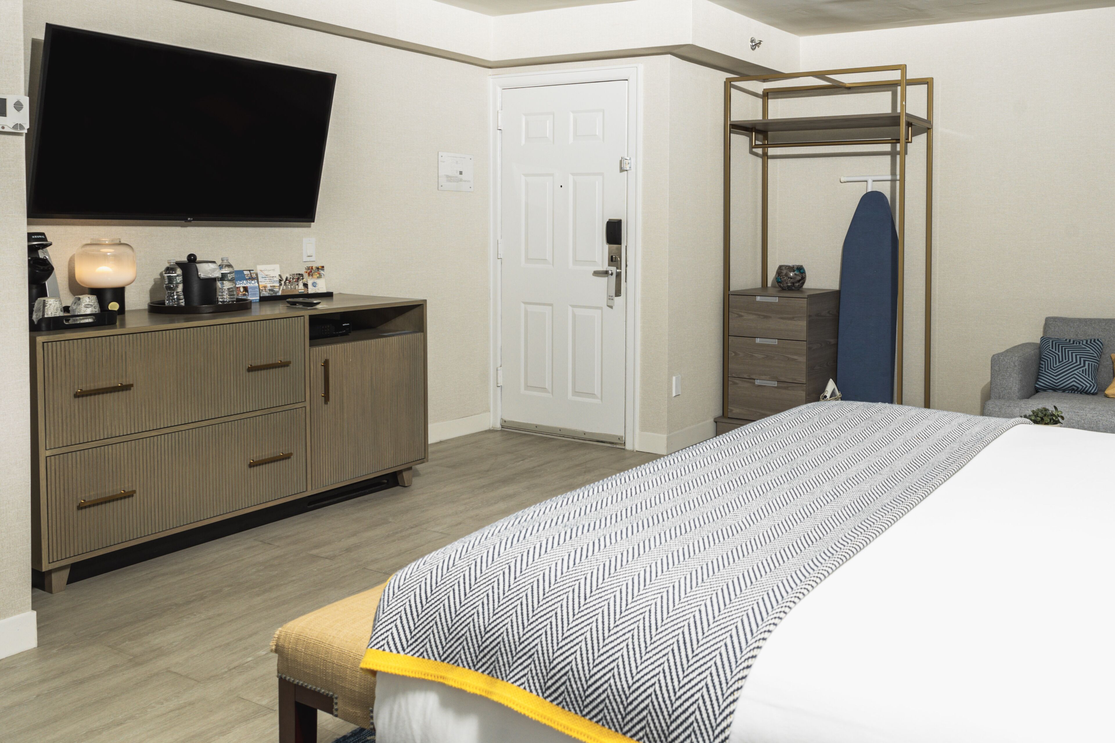 A hotel room with a bed, a TV, a wardrobe, a desk with a lamp, and a mirror.