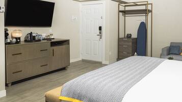 A hotel room with a bed, a TV, a wardrobe, a desk with a lamp, and a mirror.