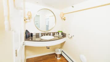 Un baño con un lavabo blanco, un espejo redondo, un perchero y un cubo de basura.