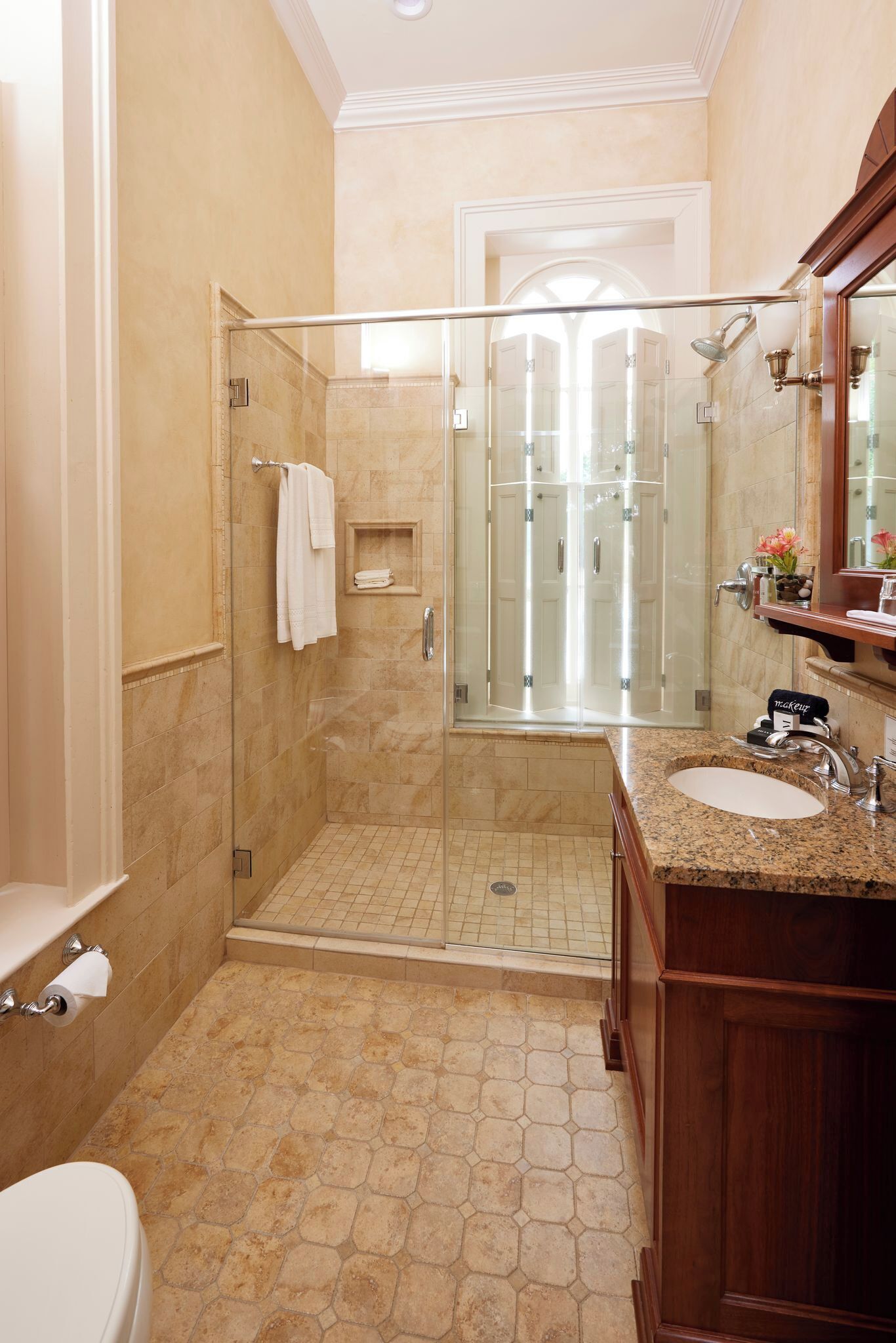 Un baño moderno con ducha envuelta en cristal, piso de baldosas de mármol y tocador de madera con lavamanos.