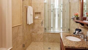 Un baño moderno con ducha envuelta en cristal, piso de baldosas de mármol y tocador de madera con lavamanos.