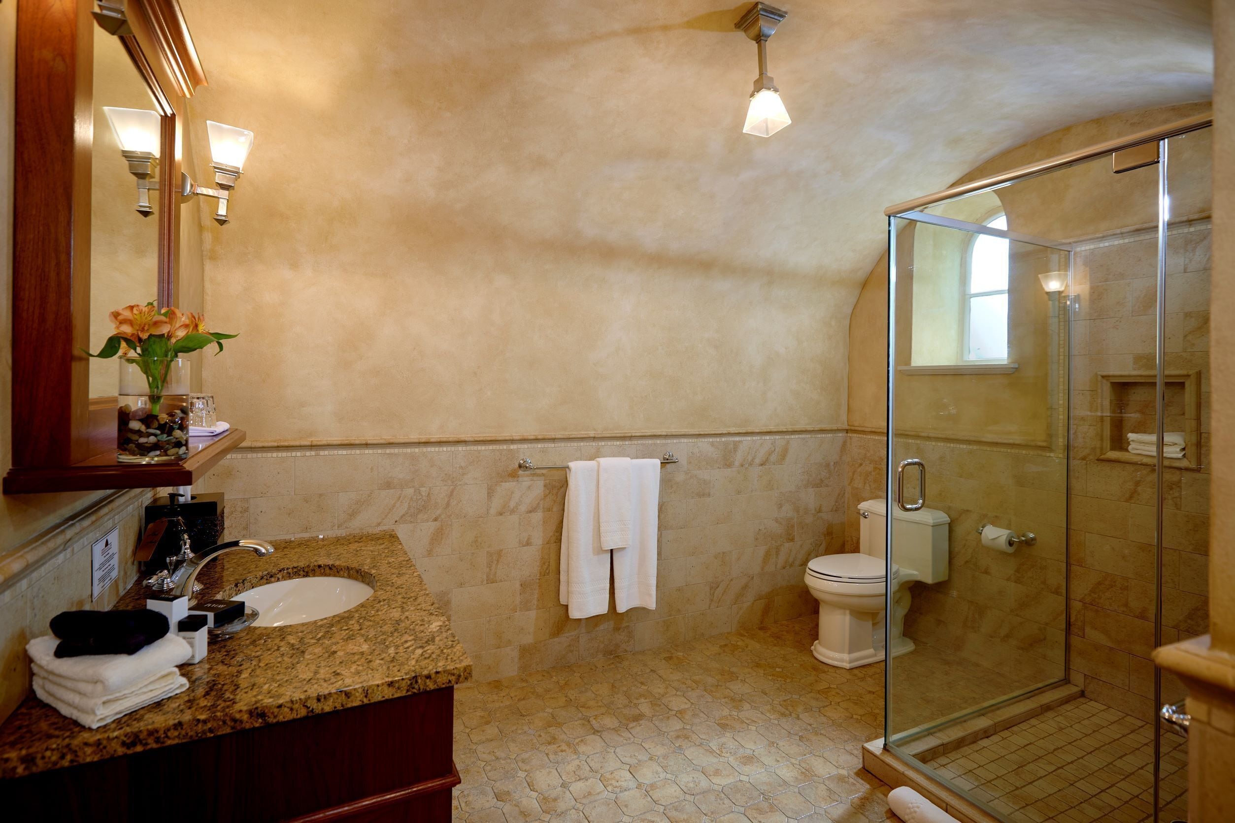 A bathroom with a granite countertop, a sink, a toilet, and a glass-enclosed shower.