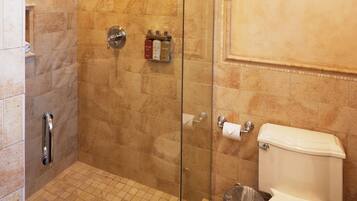 A bathroom with a glass-enclosed shower, a toilet, and a trash can.