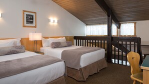 A hotel room with two beds, a desk, and a chair. There is a window with curtains and a wooden staircase. - Rocky Mountain Ski Lodge (Canmore)