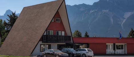 Un edificio con techo inclinado, balcón y un estacionamiento con coches.