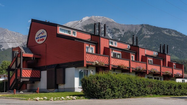 A red building with a ski lodge sign, multiple windows, and a mountain backdrop. - Rocky Mountain Ski Lodge (Canmore)