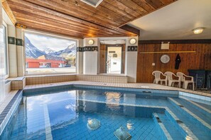 A swimming pool with a view of mountains, wooden ceiling, and a door leading outside.