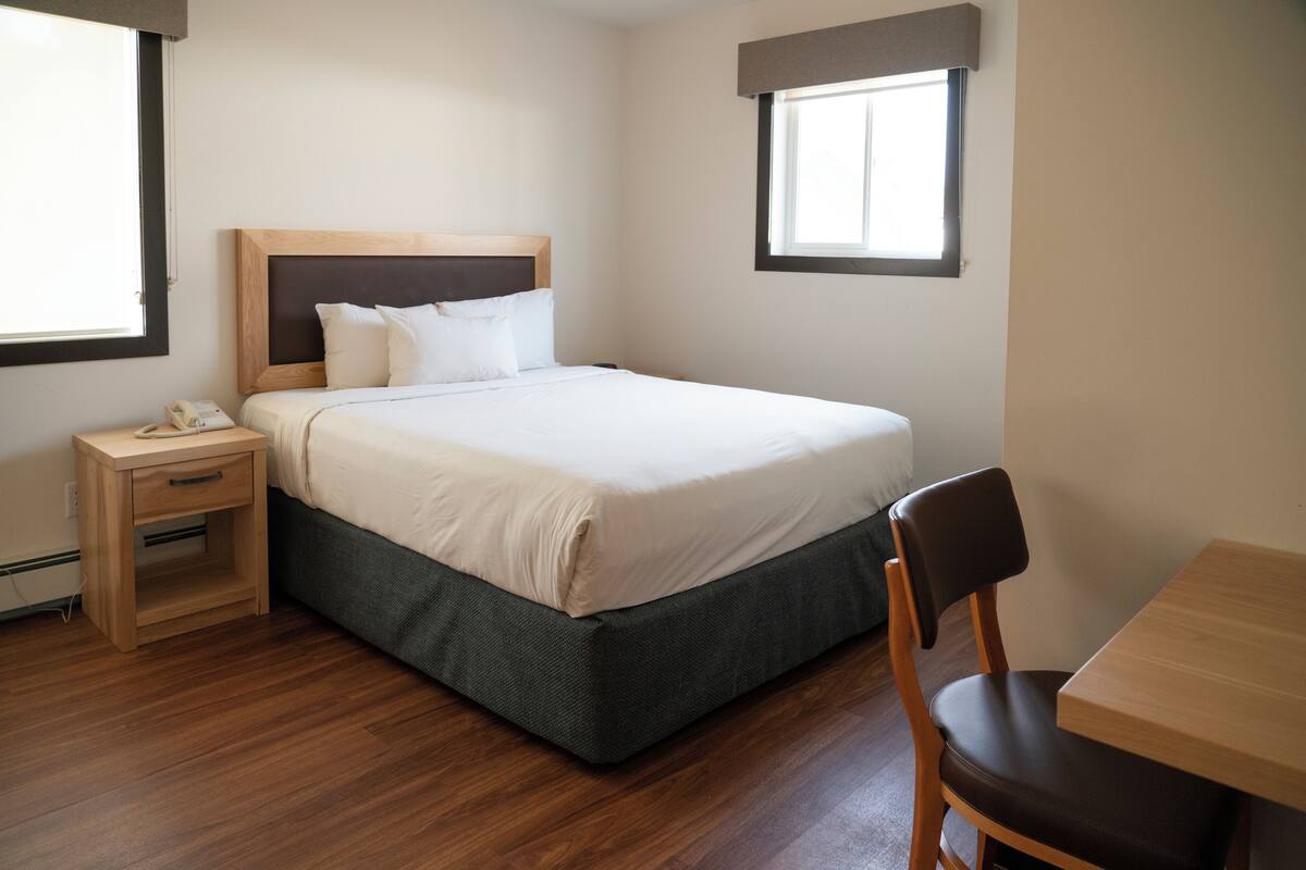 Habitación de hotel impecable con una cama individual, una mesita de noche de madera, una mesa y una silla.