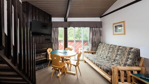 A cozy living room with a sofa, a table, and chairs, a fireplace, and a television. - Rocky Mountain Ski Lodge (Canmore)
