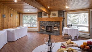A dining area with a stone fireplace, wooden tables, and a view of snow-covered trees. - Rocky Mountain Ski Lodge (Canmore)