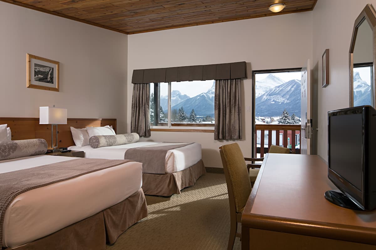 Habitación de hotel con dos camas, un escritorio, un televisor y una ventana con vista a la montaña.