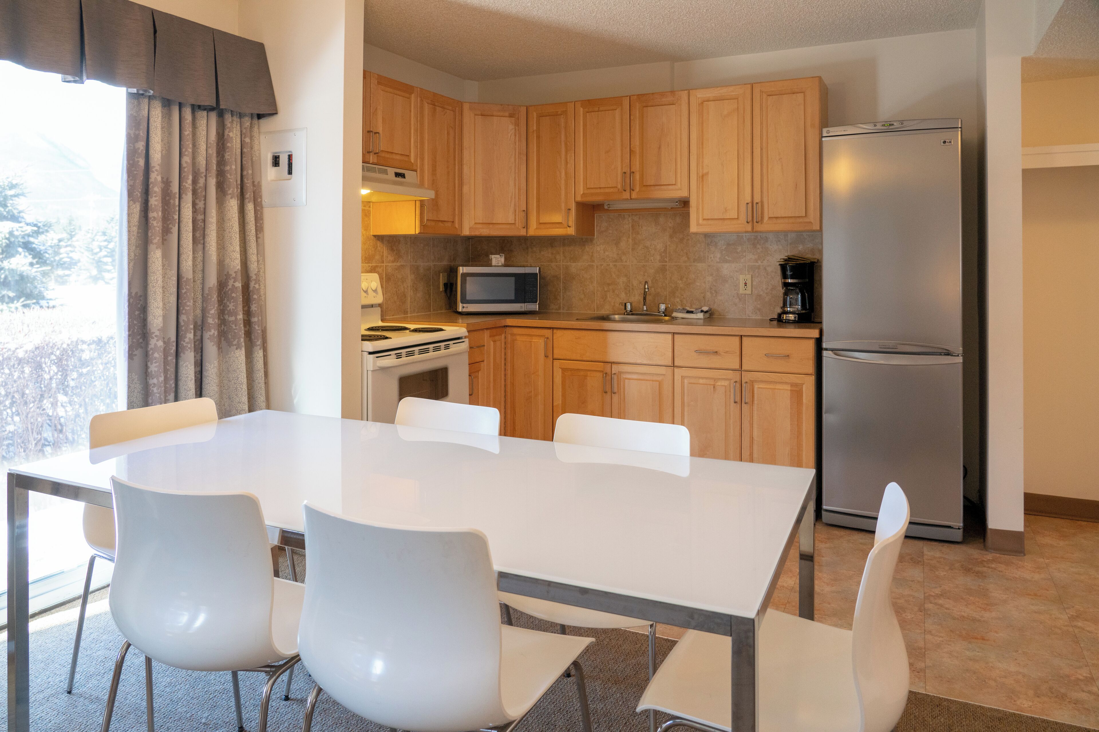 Una cocina moderna con armarios de madera, un refrigerador de acero inoxidable, un microondas y una estufa. Hay una mesa de comedor con sillas blancas.