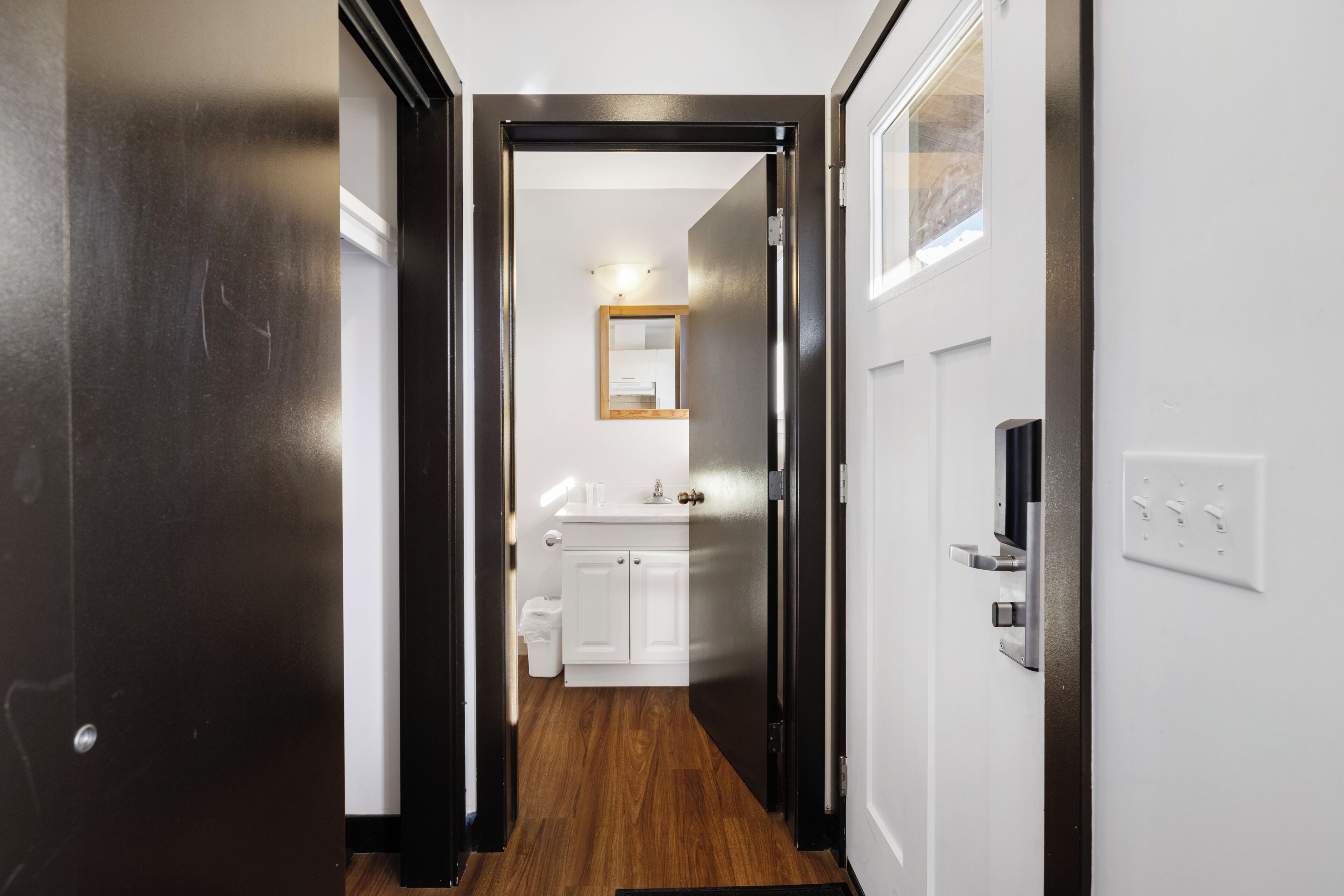 Pasillo que conduce a un baño con un lavamanos y un espejo blancos.