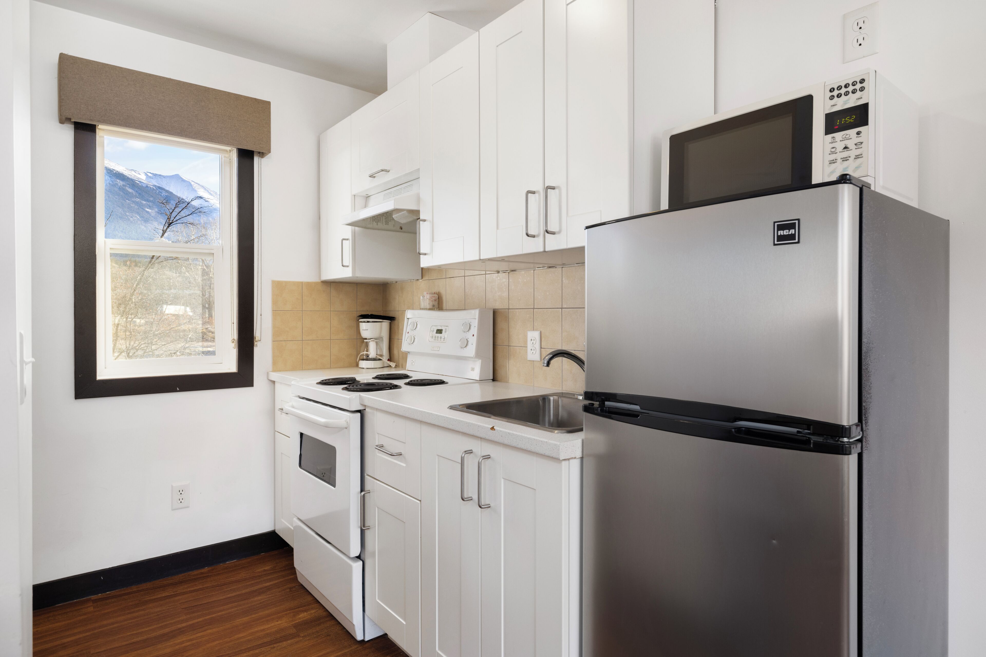 A modern kitchen with white cabinets, a stainless steel refrigerator, a built-in oven, and a coffee maker.
