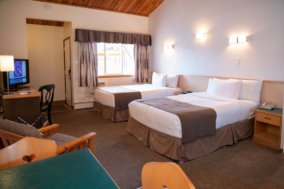 Habitación de hotel con dos camas, un escritorio con una computadora, una silla y una ventana con cortinas.