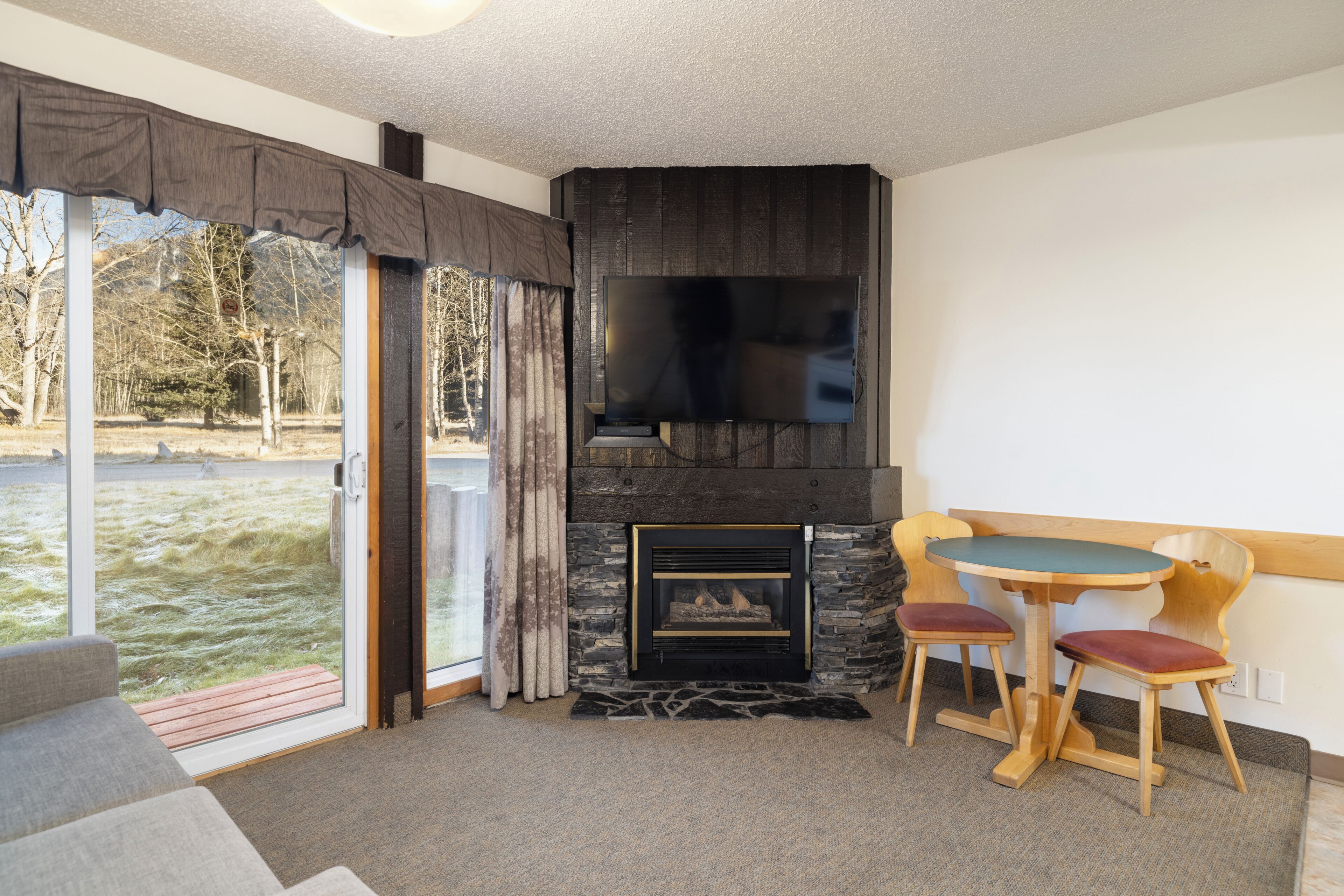 A room with a fireplace, a television, and a dining area with chairs.