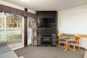 A room with a fireplace, a television, and a dining area with chairs. - Rocky Mountain Ski Lodge (Canmore)
