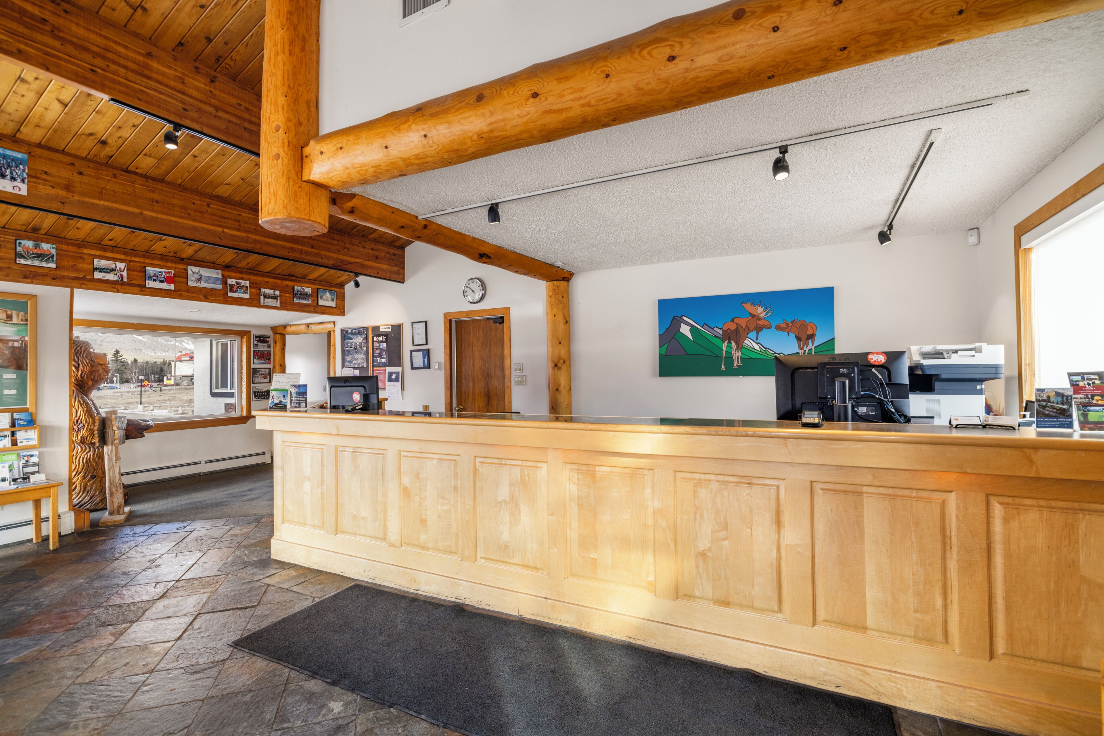 A reception area with a wooden reception desk, a clock, and a painting of moose on the wall.