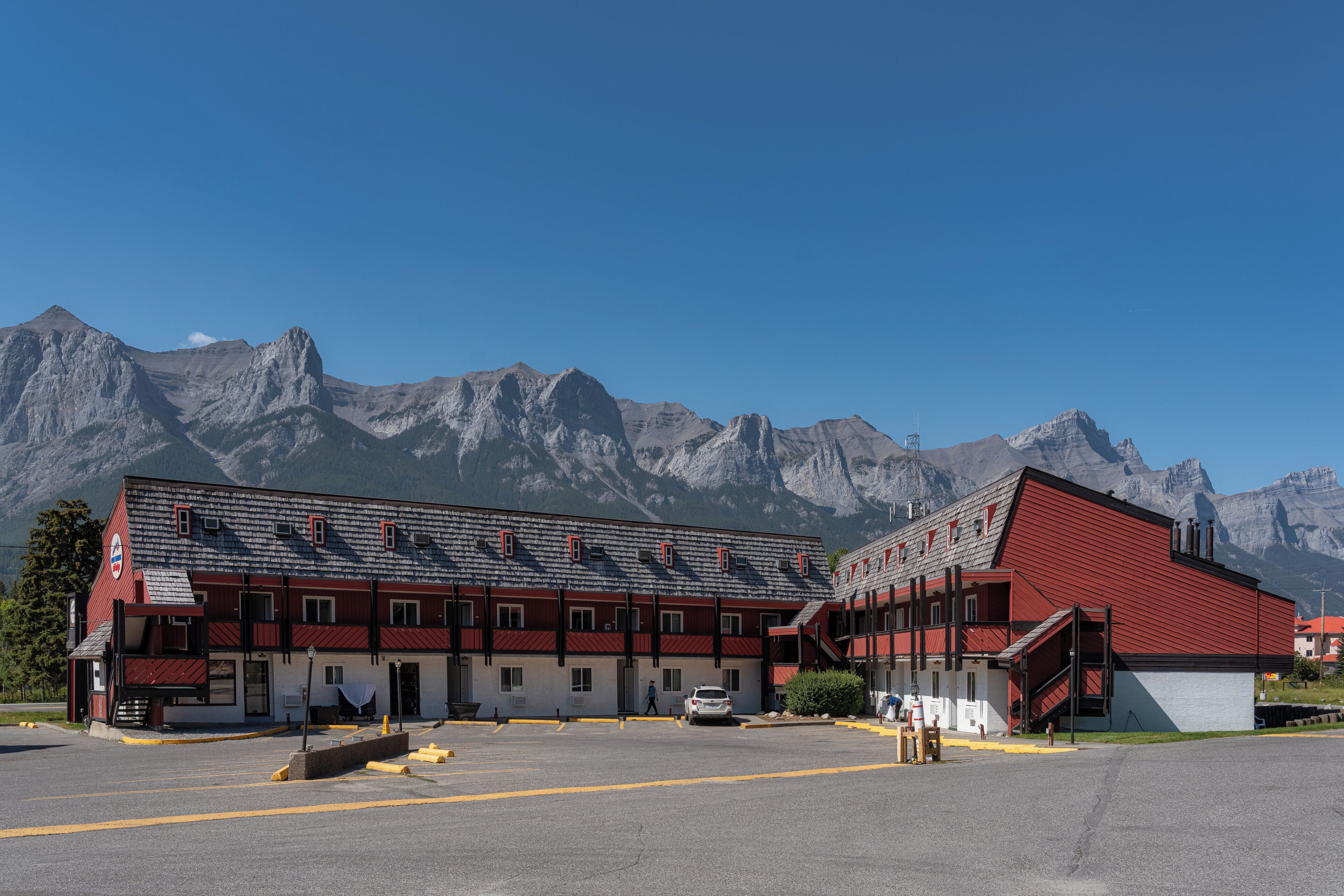 Un hôtel à la façade rouge et blanche, doté d’un parking et situé au pied d’une montagne.