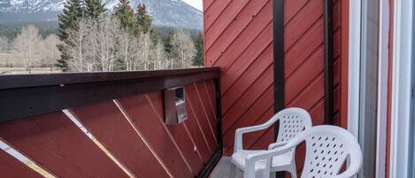 A balcony with two white plastic chairs, a red exterior wall, and a view of snow-capped mountains.