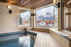 A pool area with tiled walls and a wooden ceiling, large windows offering a view of mountains and a red building. - Rocky Mountain Ski Lodge (Canmore)