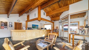 A wooden interior with a reception desk, seating area, and a view through a glass door. - Rocky Mountain Ski Lodge (Canmore)