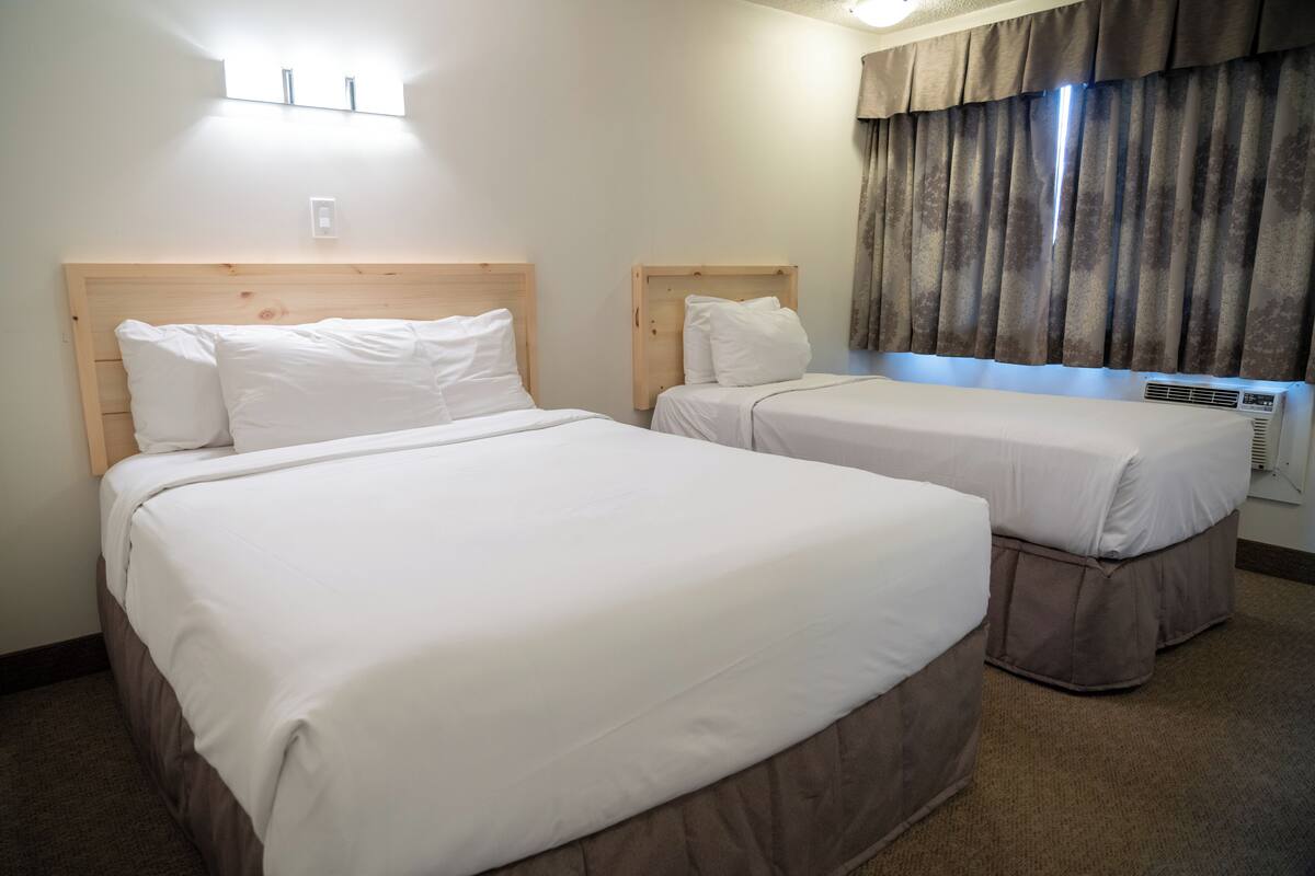 Habitación de hotel con dos camas individuales, cabecero de madera, ventana con cortinas y un aplique de pared.