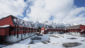 A hotel with red and white exterior walls, a parking area with snow, and a mountain backdrop. - Rocky Mountain Ski Lodge (Canmore)