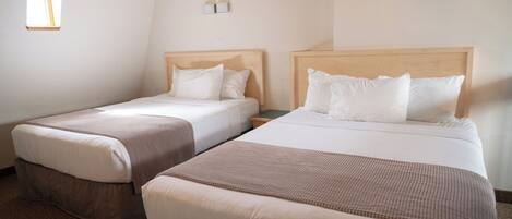 Dos camas individuales con cabeceros de madera, ropa de cama blanca y una ventana pequeña a la izquierda.