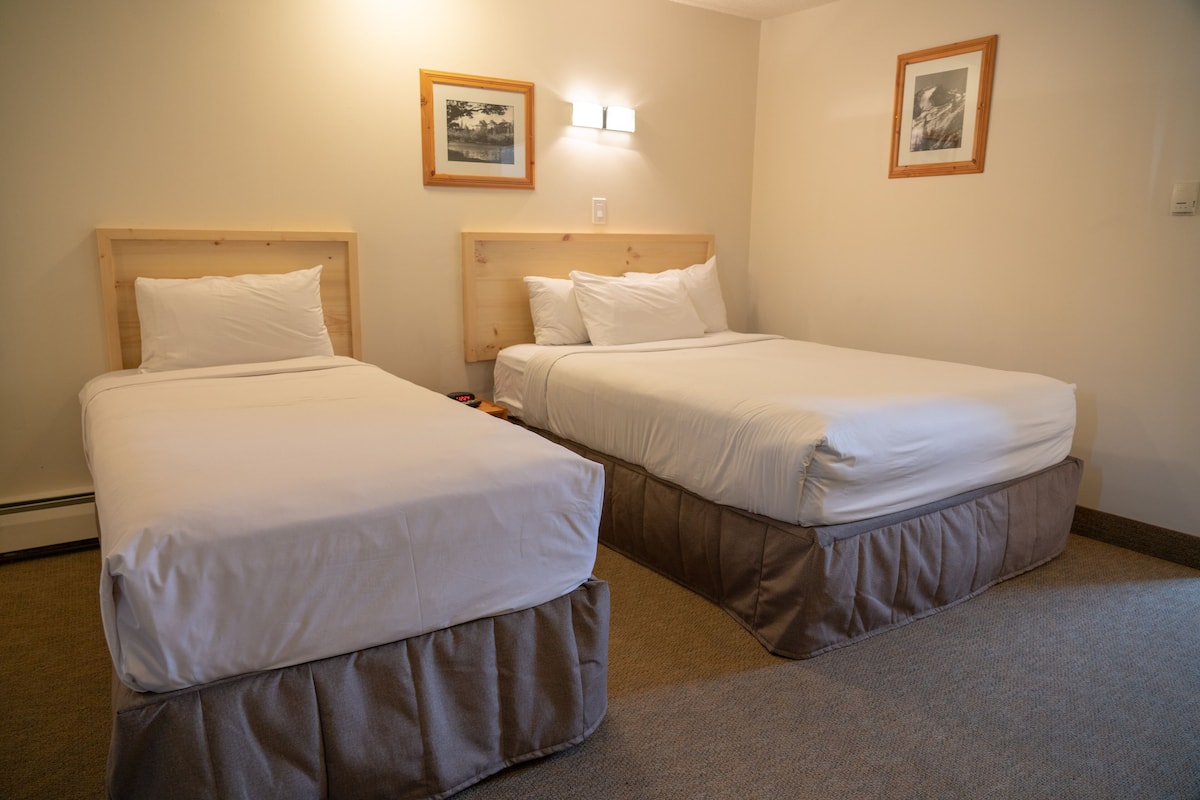 Dos camas individuales con cabeceros de madera y ropa de cama blanca en una habitación con paredes color beige y alfombra.