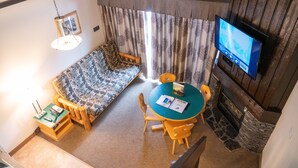 A cozy living area with a sofa, a round table, and chairs, a fireplace, and a television mounted on the wall. - Rocky Mountain Ski Lodge (Canmore)