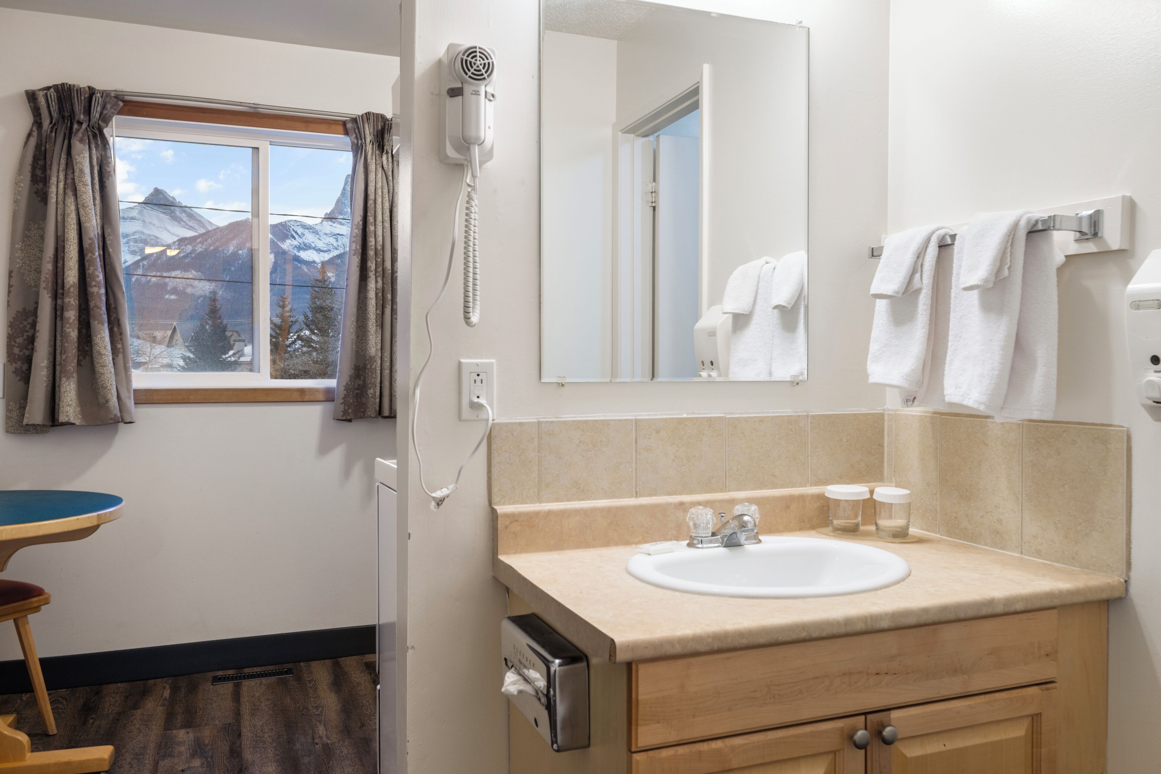 A bathroom with a window, a hairdryer, a sink, and a mirror.