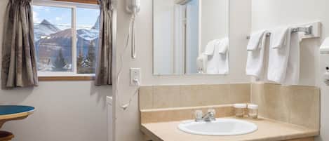 A bathroom with a window, a hairdryer, a sink, and a mirror.