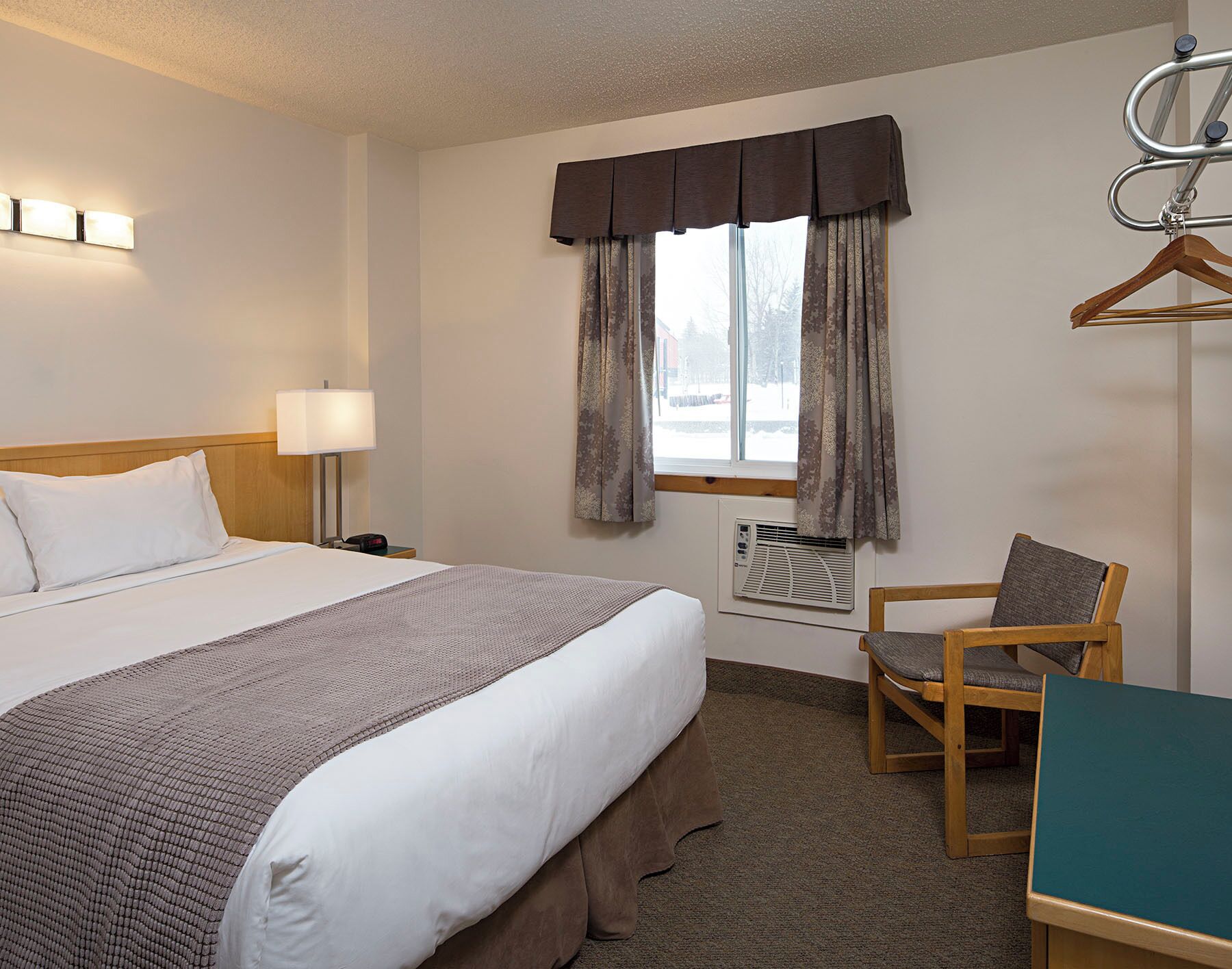 Une chambre d’hôtel comprenant un lit, une lampe de chevet, une fenêtre avec des rideaux, une chaise et un bureau.