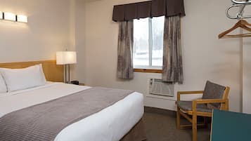 Une chambre d’hôtel comprenant un lit, une lampe de chevet, une fenêtre avec des rideaux, une chaise et un bureau.
