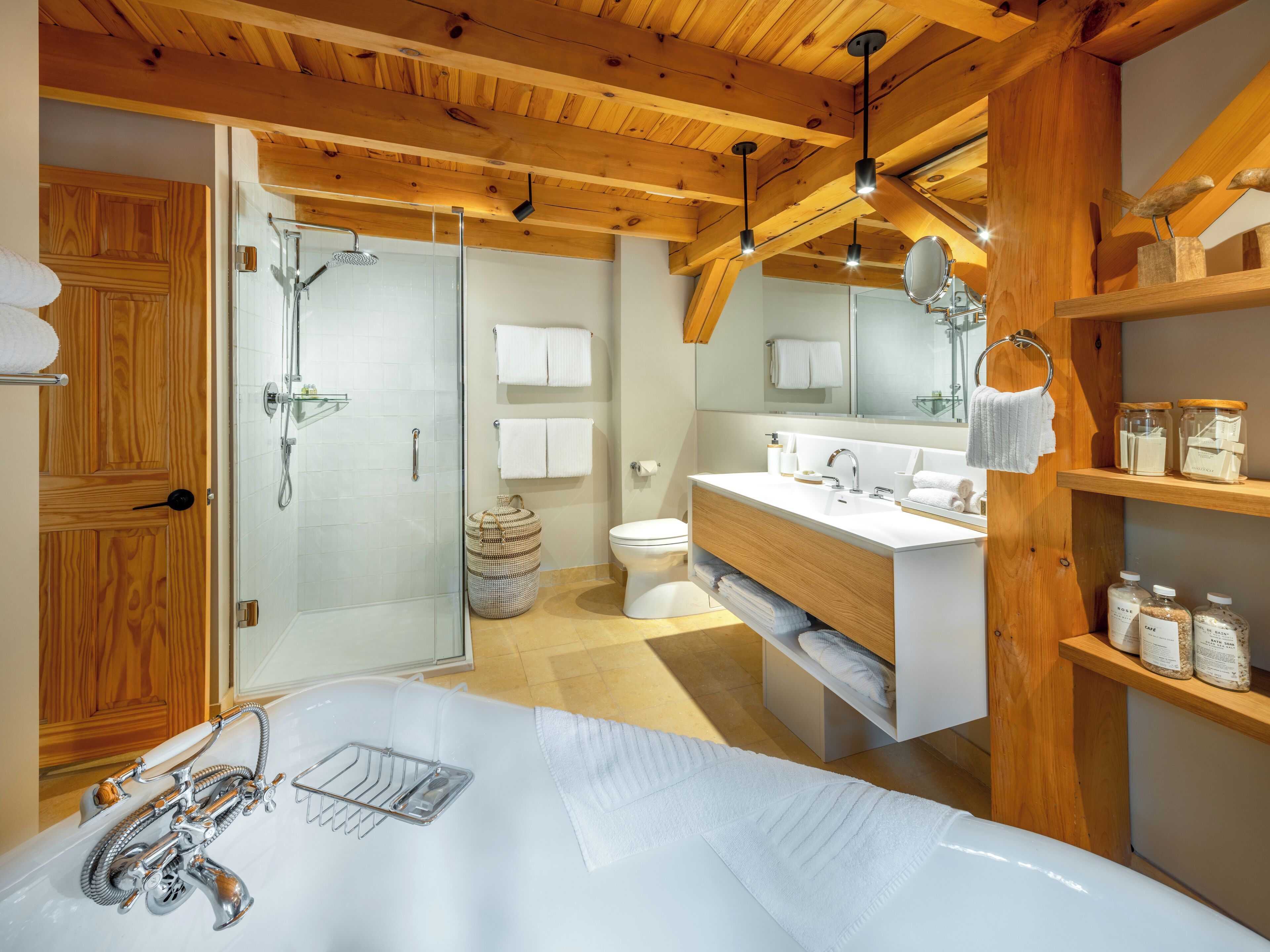 A modern bathroom with a glass shower, a white sink, and wooden beams on the ceiling.
