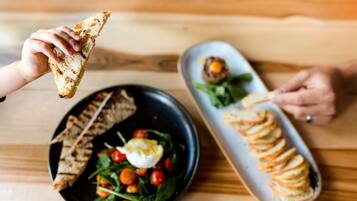 A dining table with a black plate containing a salad with cherry tomatoes and a poached egg, and a white plate with a stack of bread slices and a small dish of sauce.